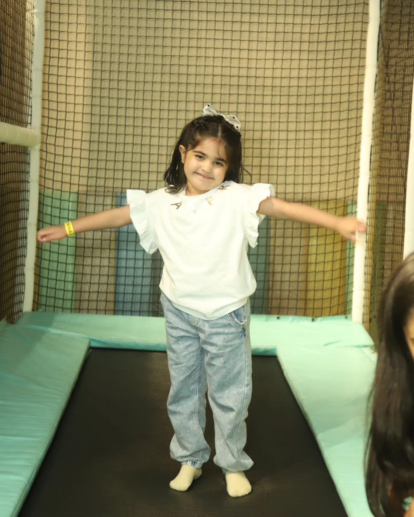 Young girl smiling with arms outstretched while standing on a padded trampoline at Chhatarpur play area