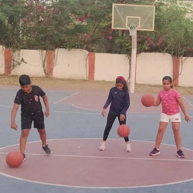 Children playing basketball on an outdoor court with trees and a fence in the background.