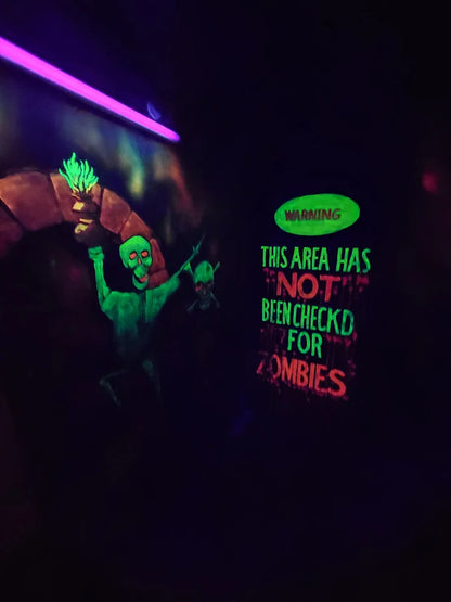 Neon-lit mural of a monster and skeletons with a "Warning: This area has not been checked for zombies" sign.