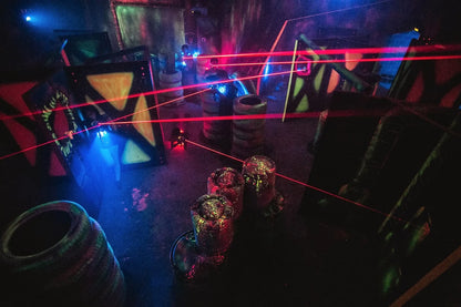 Laser tag arena with players and red laser beams crisscrossing the dark, neon-lit space.