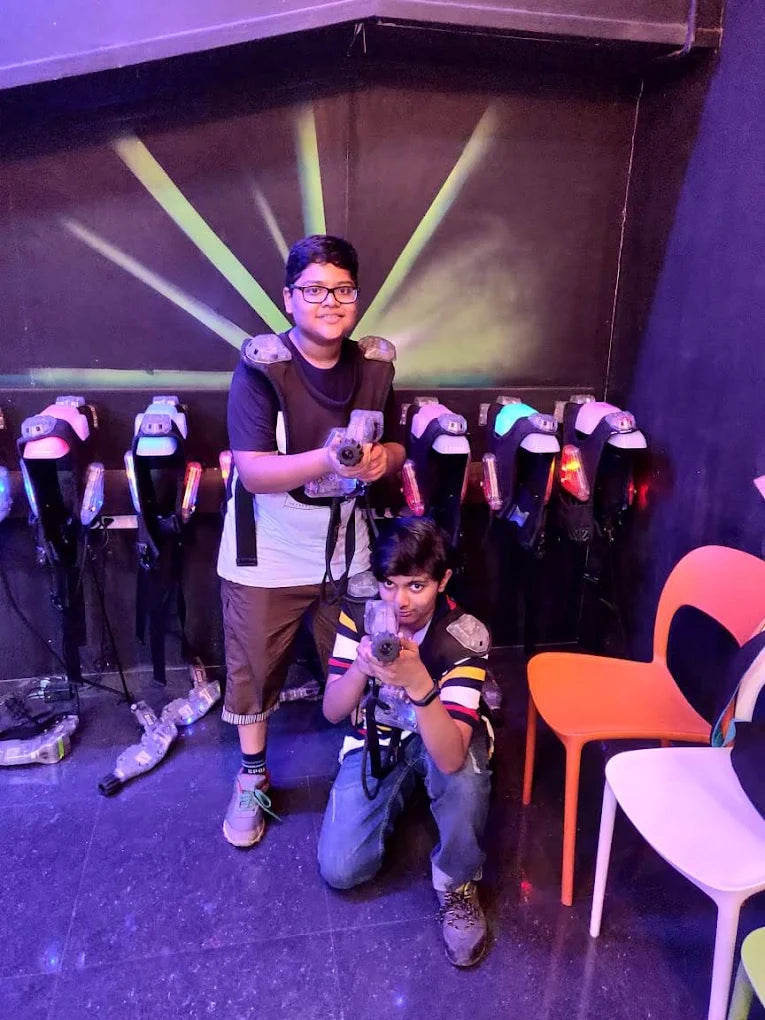 Two young boys in a laser tag arena, wearing vests and holding phasers.