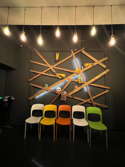 Five colorful chairs are arranged in front of a wall decorated with wooden planks and masks.