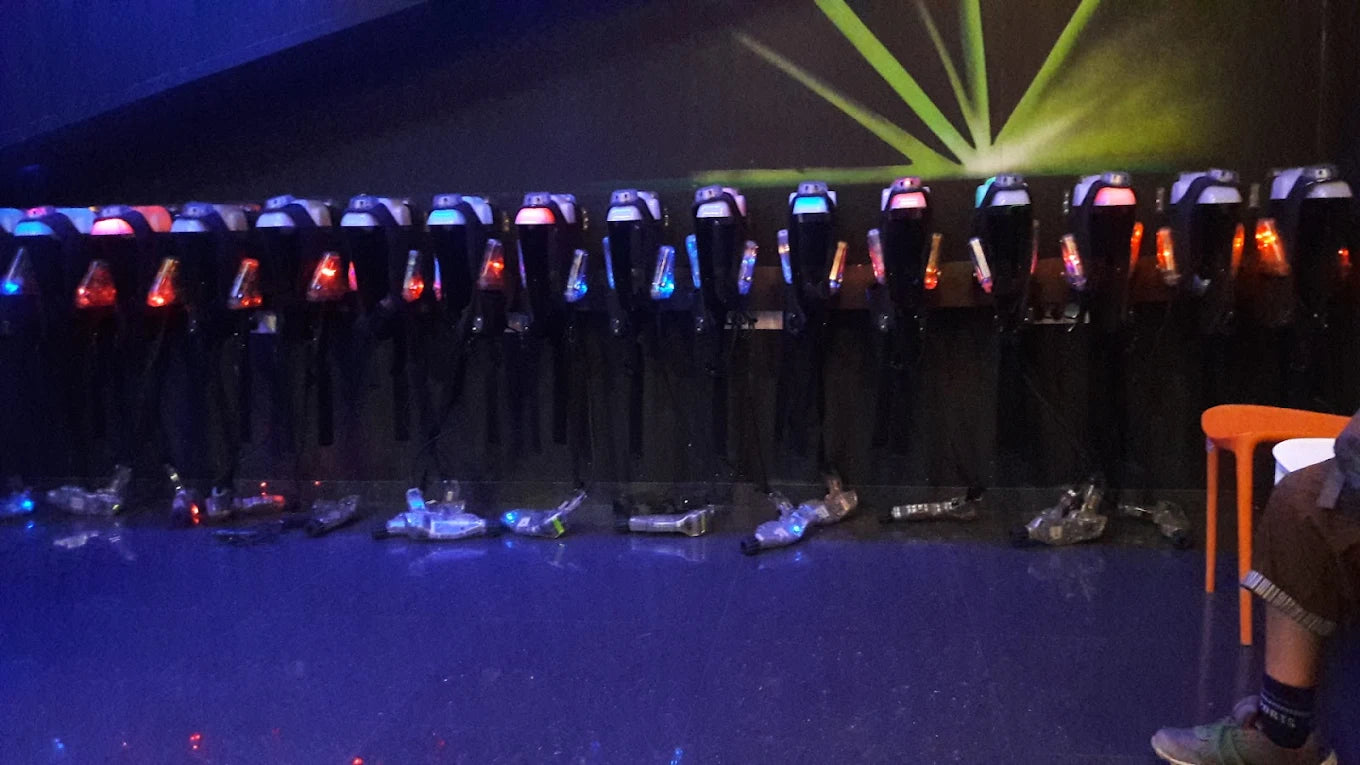 Laser tag phasers are lined up in a dark room with neon lights.