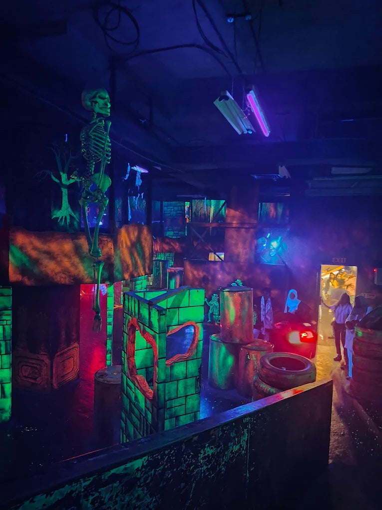 A dimly lit laser tag arena with neon-green obstacles and a hanging skeleton.