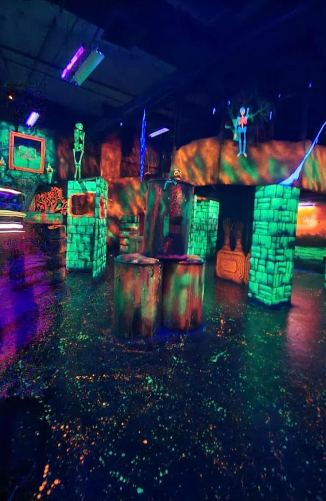 A dark, neon-lit laser tag arena with glowing obstacles and skeletons.
