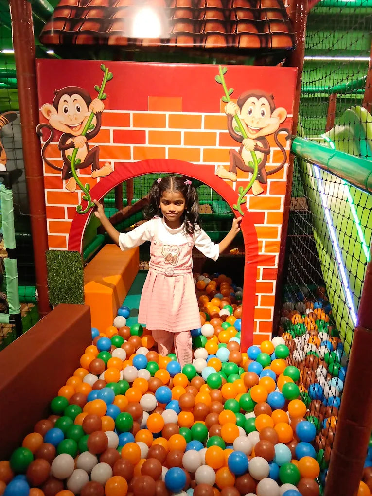 A young girl stands in a ball pit in a colorful indoor playground with monkey decorations.
