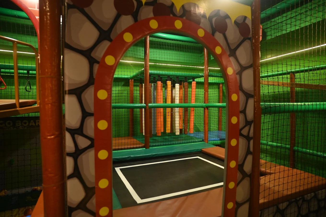 A colorful indoor playground with a trampoline and climbing structures for children.
