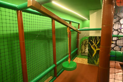A jungle-themed indoor playground with a rope swing and climbing wall for children.