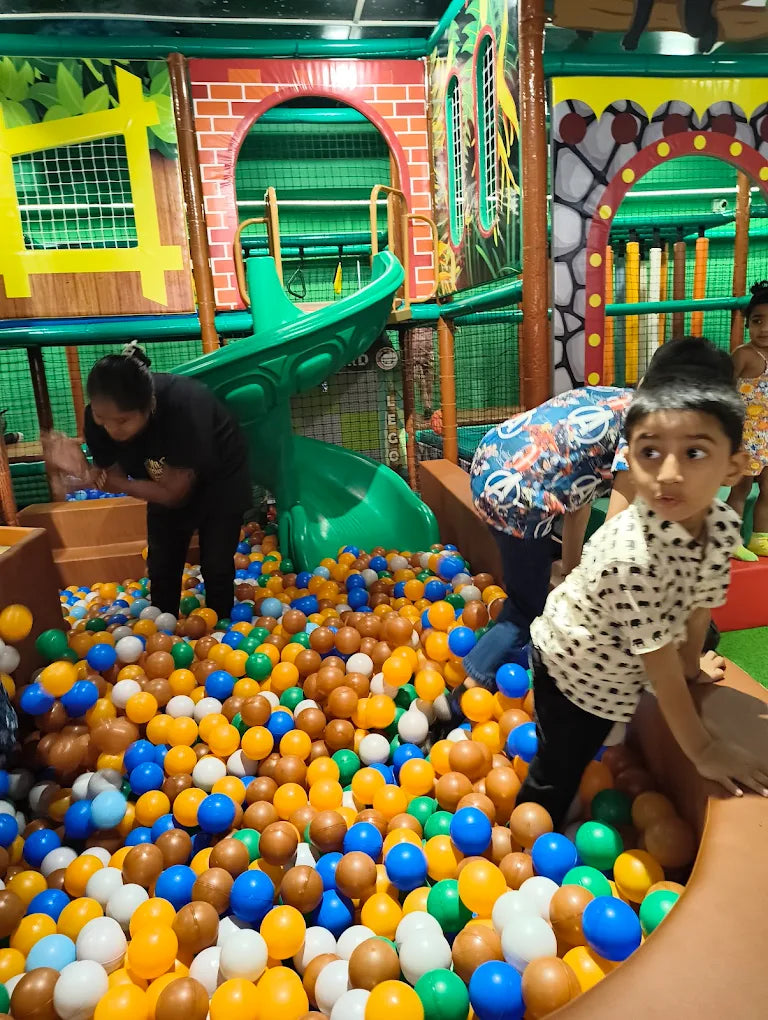 Children play in a colorful ball pit in an indoor playground.