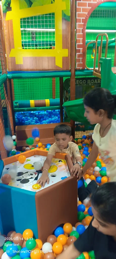 Children play in a colorful indoor playground with a ball pit and a game table.