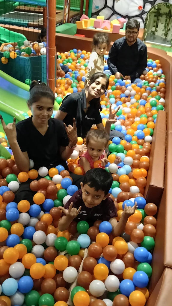 A group of children and adults play in a ball pit at an indoor playground.