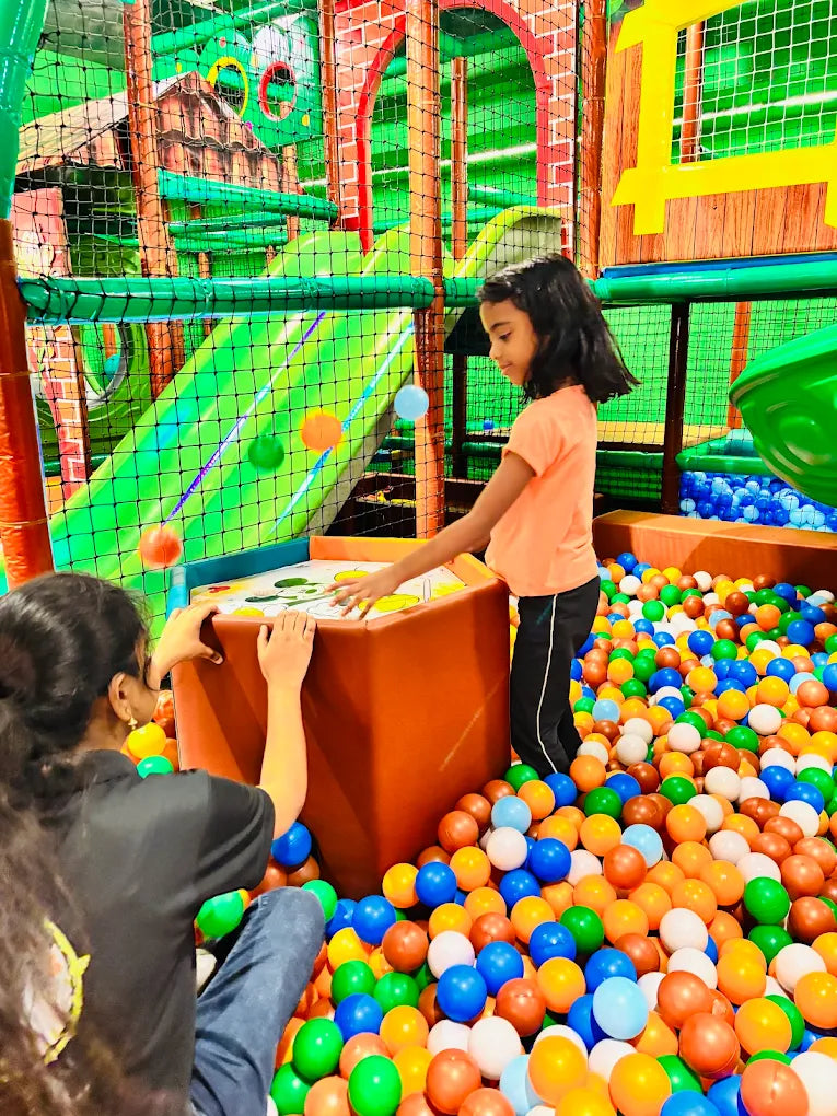 Children play in a colorful ball pit at an indoor playground.