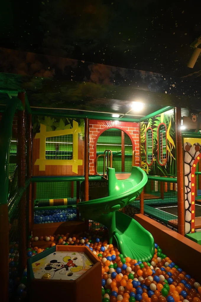 A colorful indoor playground with a ball pit, slide, and jungle-themed decorations.