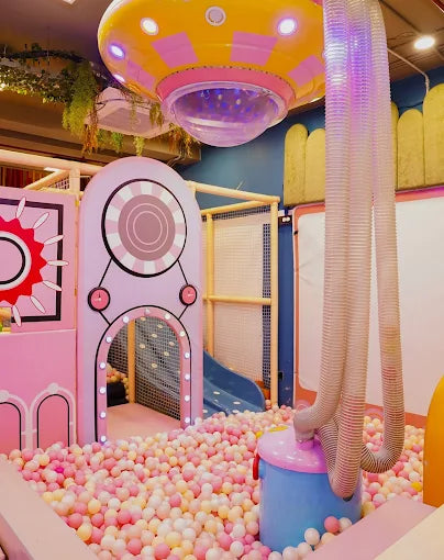 A colorful indoor playground with a ball pit, slide, and a UFO-themed structure, likely for young children.