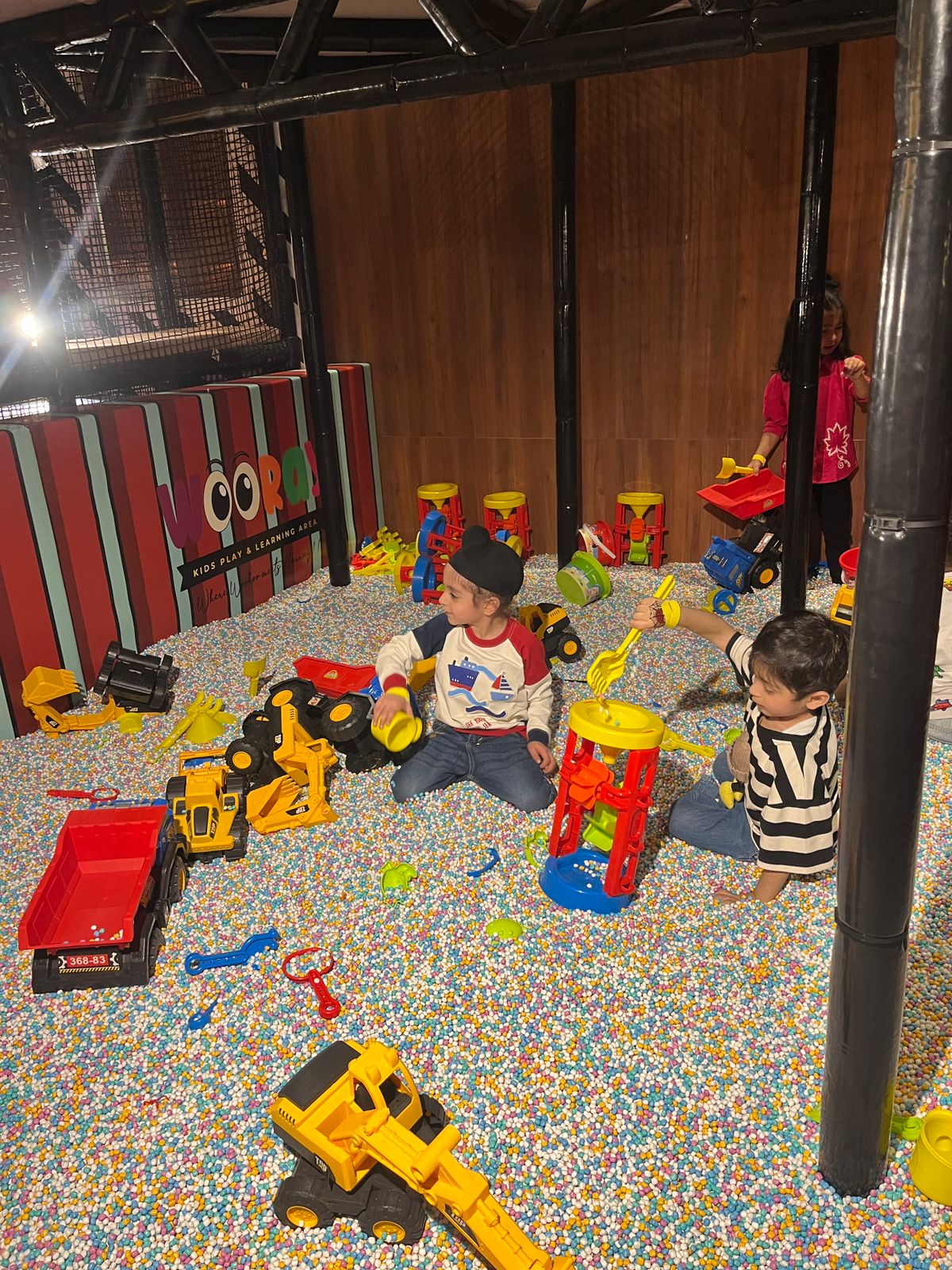Young children play with toy construction vehicles in a ball pit.