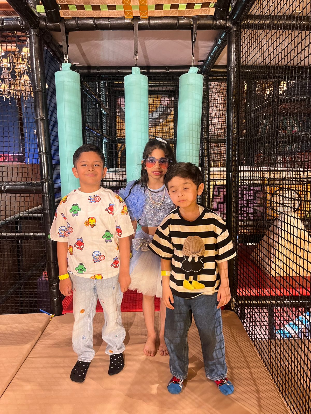 Three children pose in a colorful indoor playground.