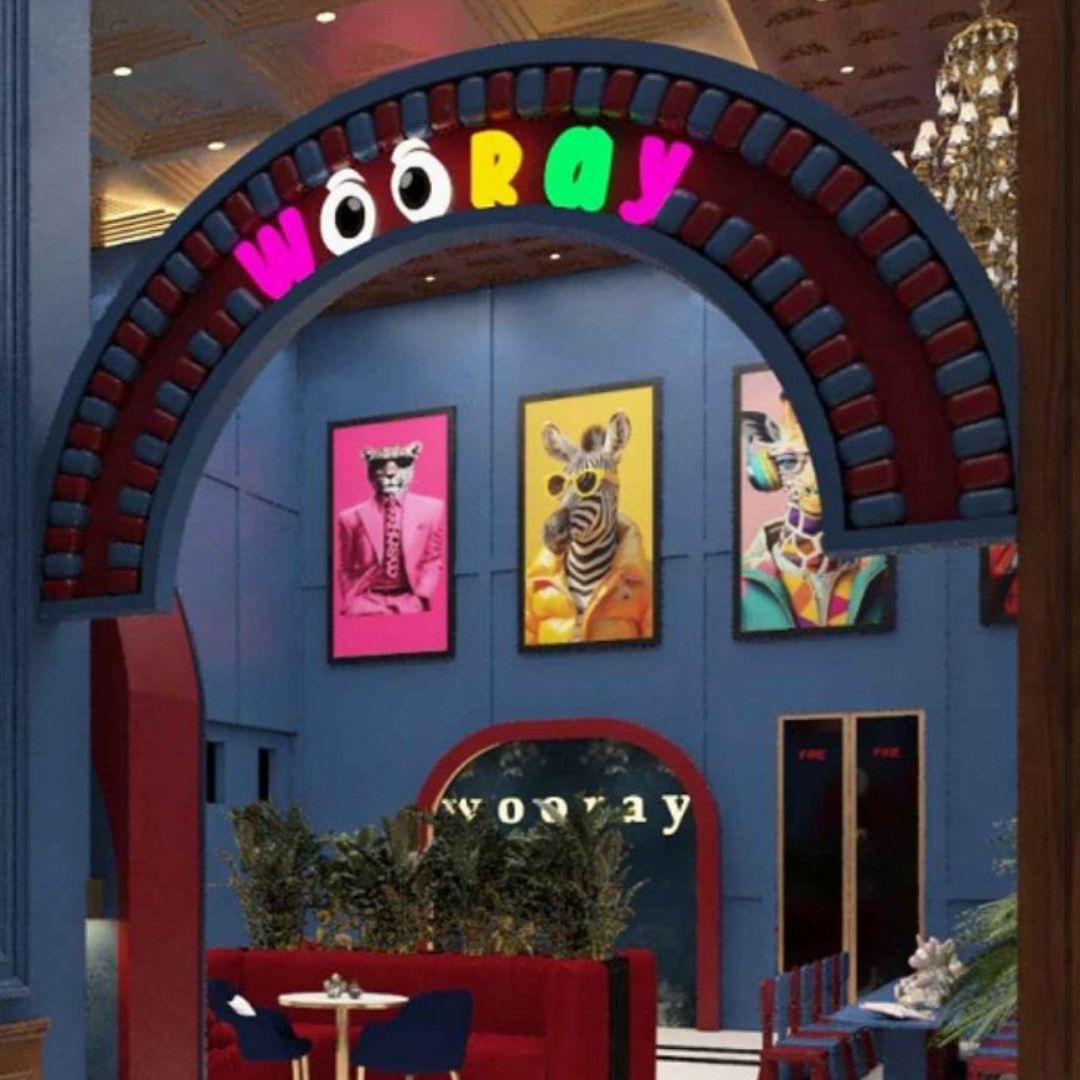 An archway with "wooray" in neon letters above a seating area with colorful animal art.
