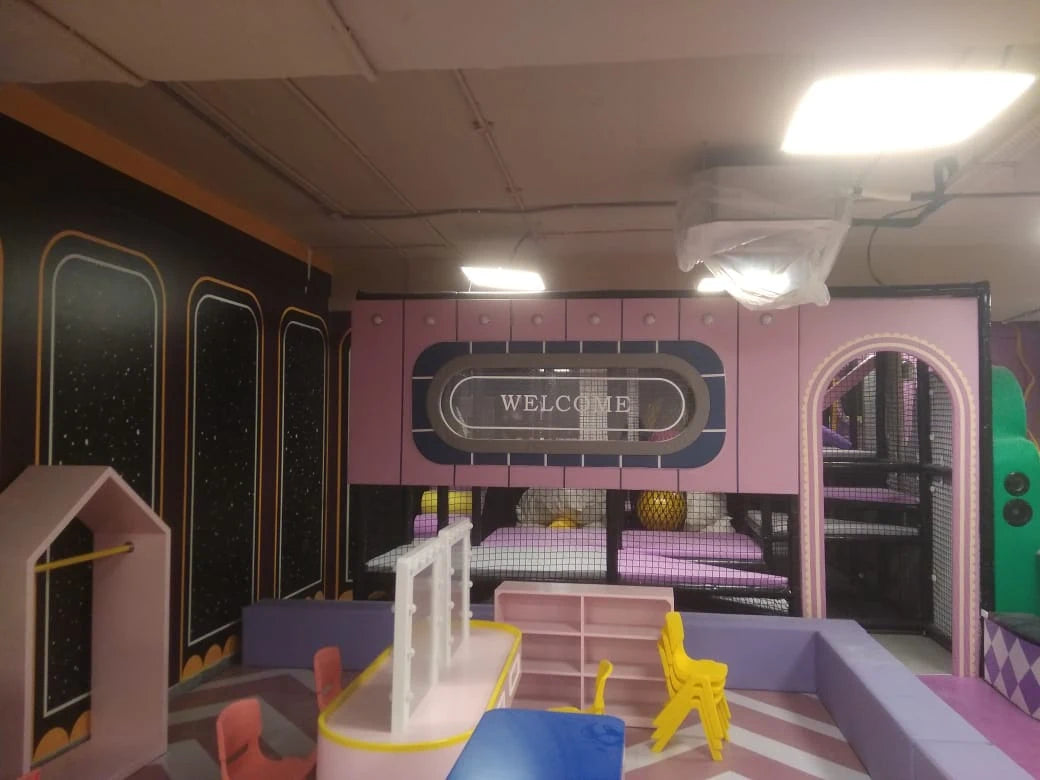 A pink and purple indoor play area for children with a "Welcome" sign and play structures.