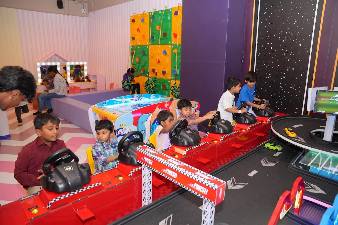 Children play a racing arcade game in a colorful entertainment center.