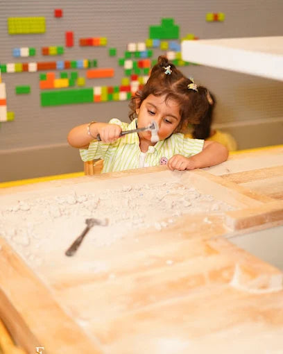 A young child plays with a toy hammer in a sandpit.