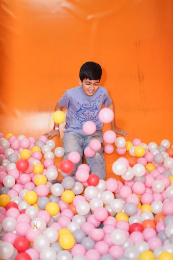 A young boy in a ball pit throws colorful balls in the air.