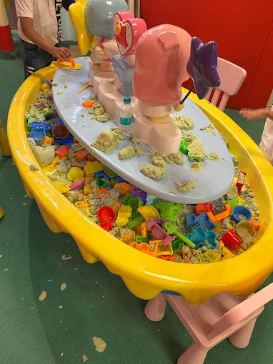 A child plays with kinetic sand and toys in a yellow sand table.