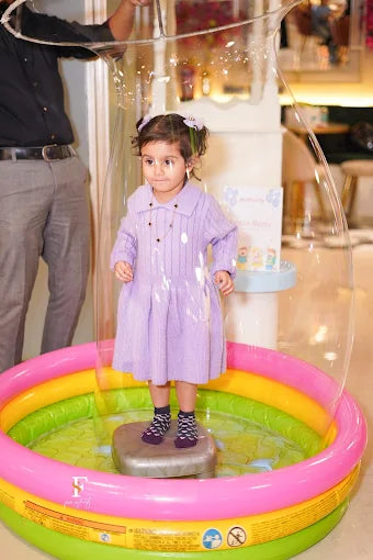 A young child stands inside a giant bubble in an inflatable pool.