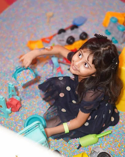 A young girl plays with colorful toys in a ball pit.