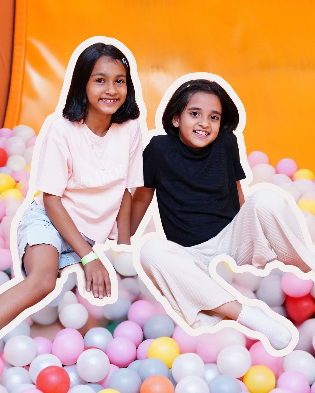 Two young girls sit in a ball pit, smiling at the camera.
