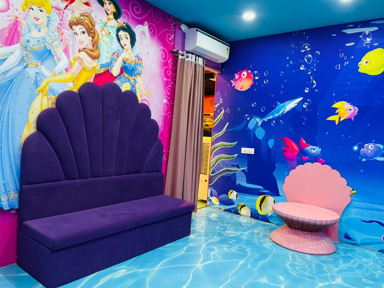 A whimsical room with princess and underwater murals, featuring purple and pink shell-shaped seating.