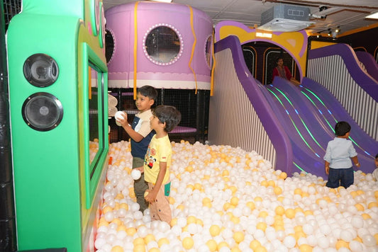 Children play in a ball pit with a purple slide and a green play structure.