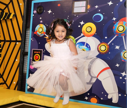 A young girl in a white tutu stands in front of a space-themed mural with an astronaut.