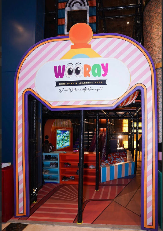 Entrance to a colorful indoor play area for children, featuring a "WOORAY" sign and a ball pit.