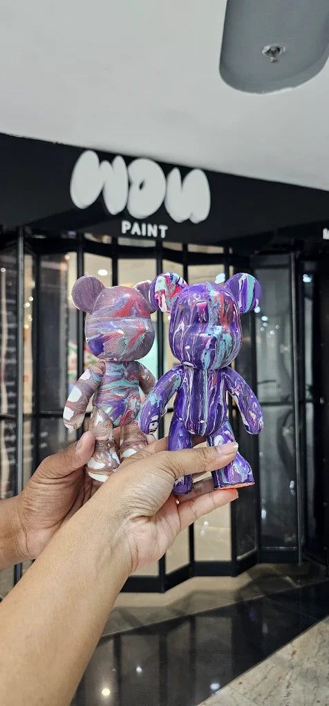 Two people hold up colorful, drippy bear figurines in front of a store called "WOW PAINT."