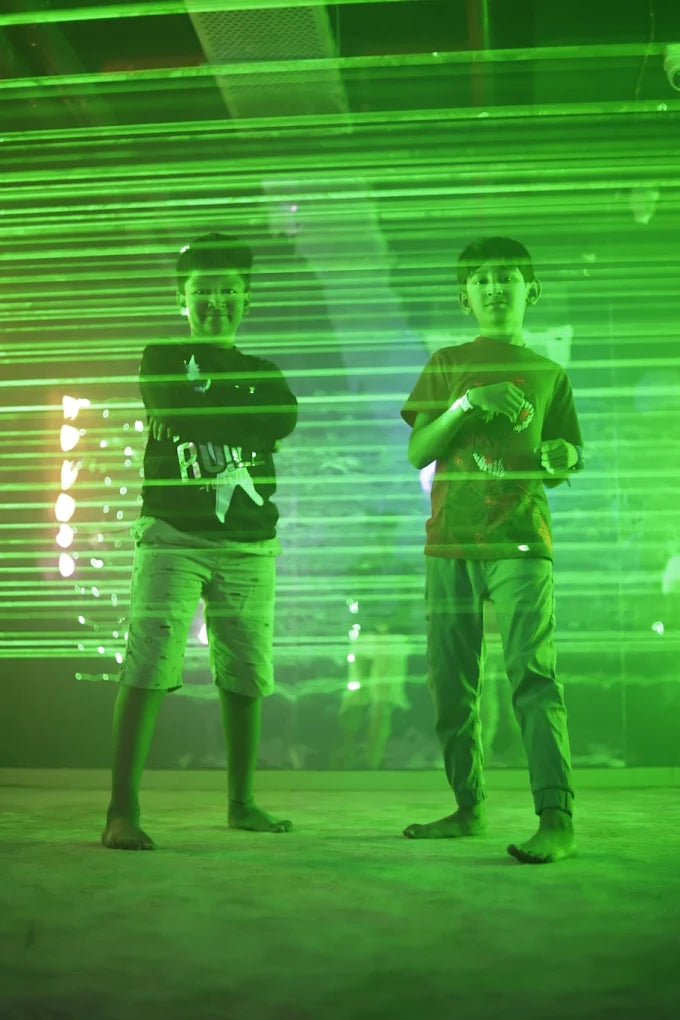 Two young boys stand in a room with green laser lights.