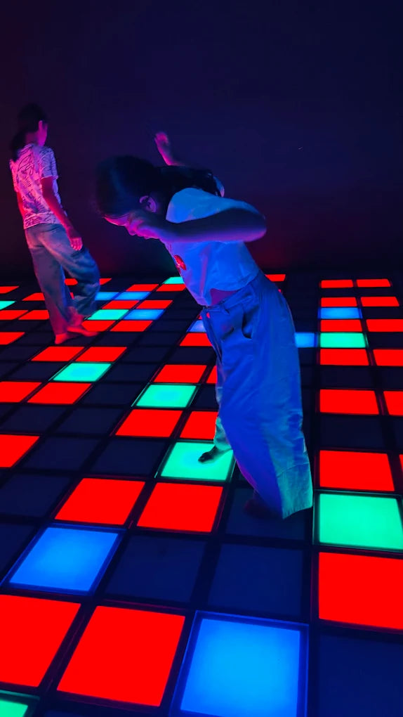 Two young people dance on a colorful, illuminated dance floor.