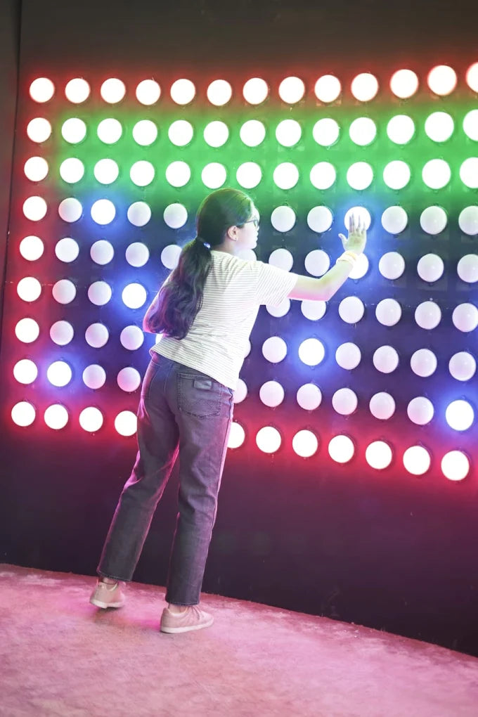 A young person interacts with a wall of colorful, illuminated buttons.