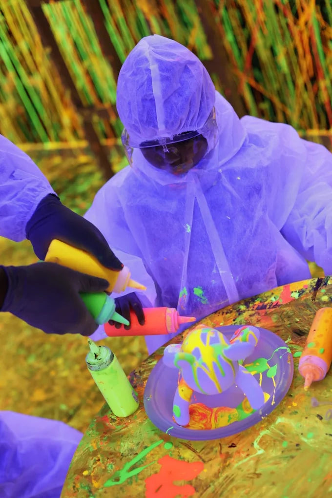 Children in protective suits paint a toy with neon colors under blacklight.