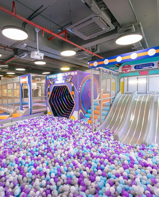 A colorful ball pit filled with children's toys, with slides and play structures in the background.