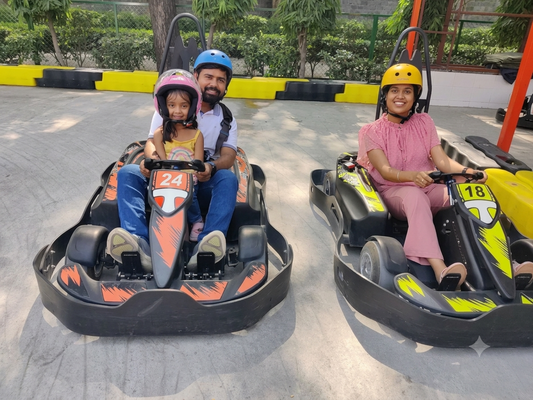 A family enjoys go-karting, with a father and daughter in one kart and a woman in another.
