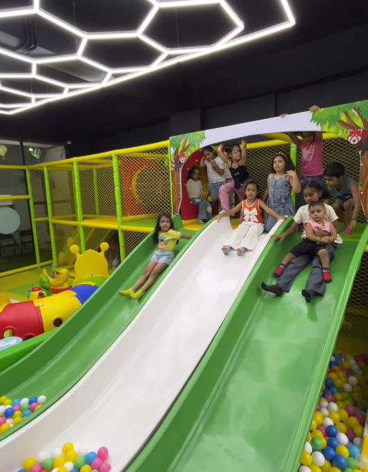Children enjoy sliding down a green and white slide at an indoor playground.