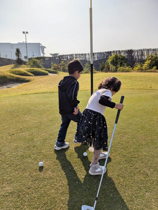 Two children on a golf course with one holding a golf club.