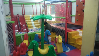 A person sits in a colorful indoor playground with slides, a ball pit, and climbing wall.