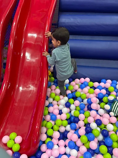 A young child climbs a red slide in a ball pit.
