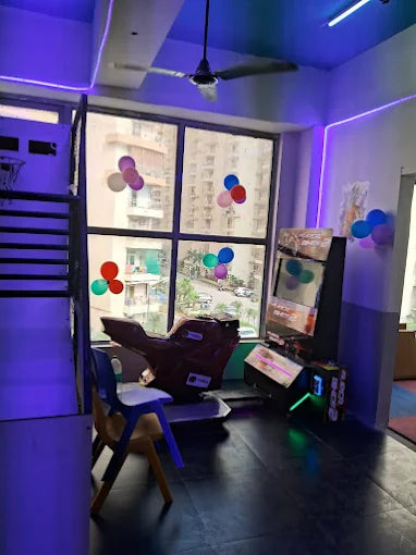 A room with a gaming machine, a motorcycle-shaped ride, and balloons, suggesting a children's party or play area.