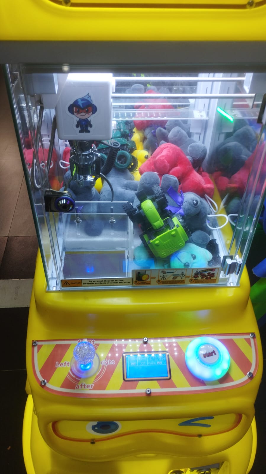 A yellow claw machine filled with stuffed animals, with a joystick and start button visible.