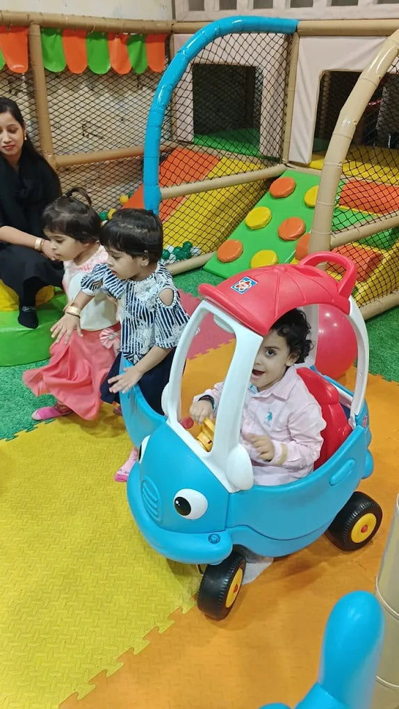 Children play in a colorful indoor playground with a toy car.