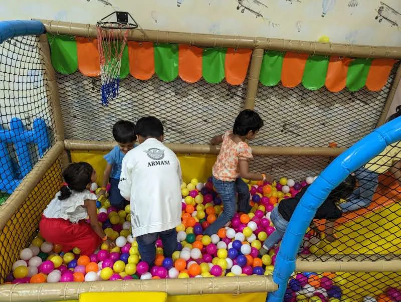Children play in a ball pit with a basketball hoop above.