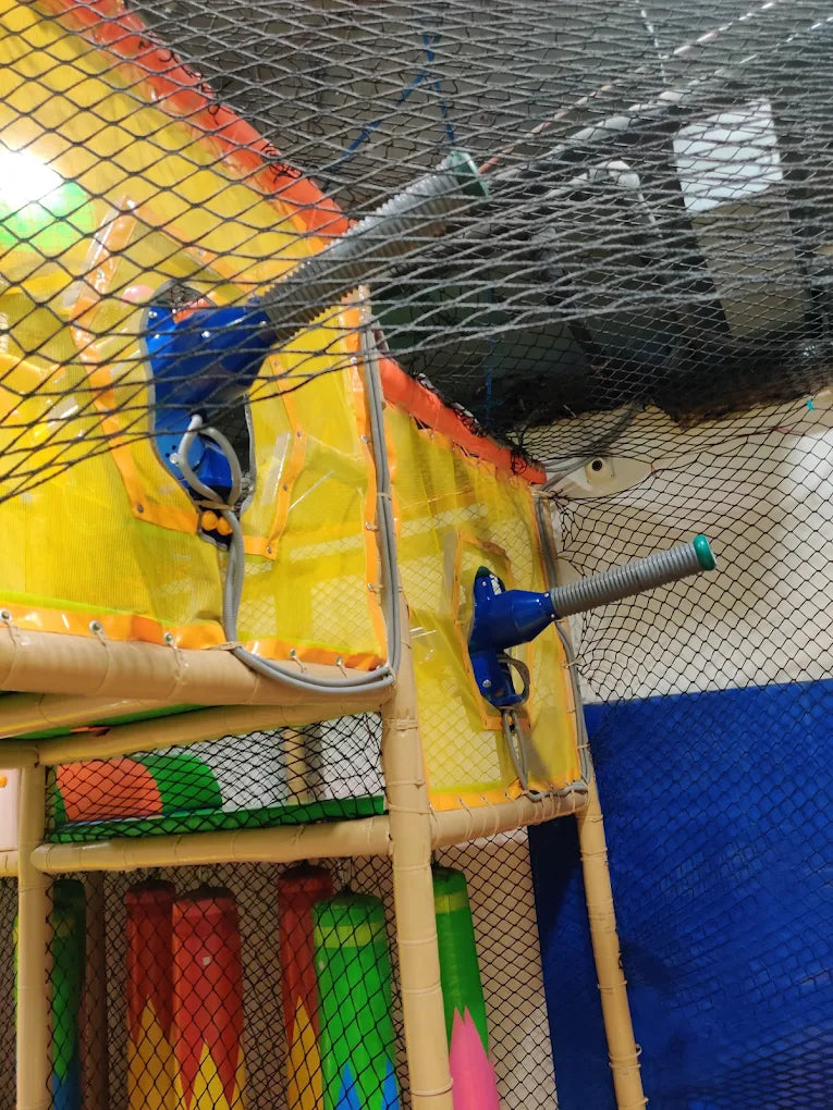 A children's indoor playground with soft play structures and netting.