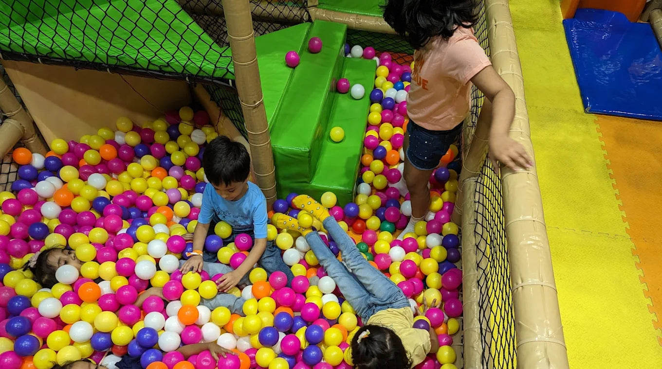 Children play in a ball pit with colorful balls and green slides.